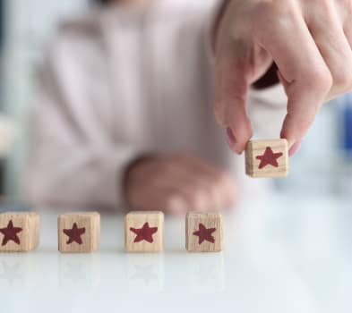 Hand places a wooden cube with a red star to complete a five-star rating row on a reflective white table.