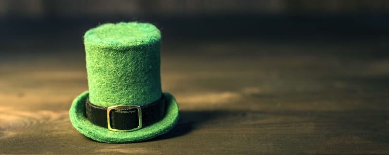 Mini green felt top hat with black band and gold buckle on a wooden surface, a St. Patrick’s Day prop.