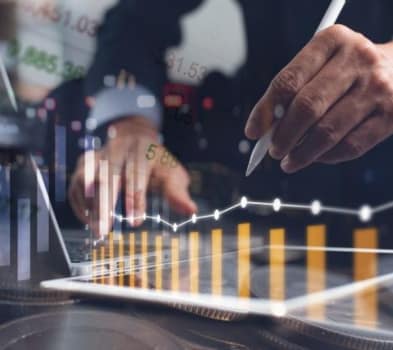 Businessperson uses stylus on a tablet beside a laptop, overlaid with rising bar and line charts signaling financial growth.