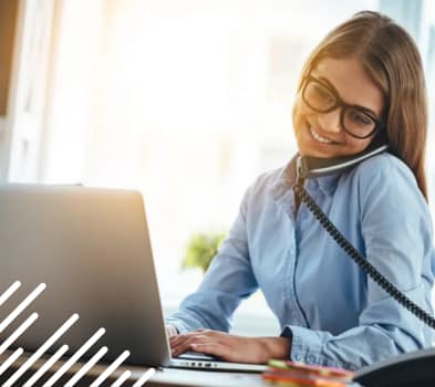 A woman sits at a desk, focused on her laptop, with a notepad and pen beside her.