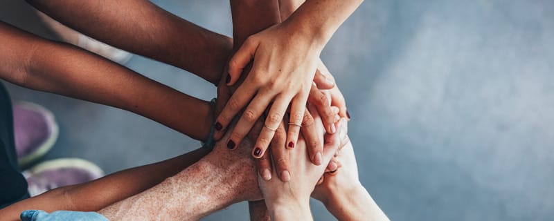 Stack of hands in a team huddle, overlapping palms from multiple people, symbolizing unity and collaboration.
